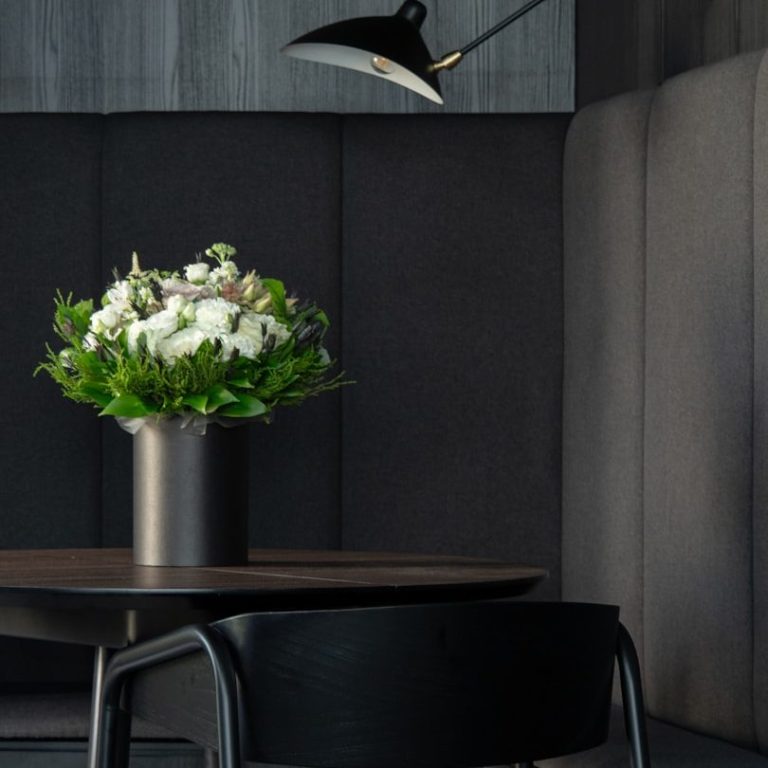 Wohnraumdetail Blumenstrauß in einer modernen Vase auf einem Tisch mit schwarzem Stuhl in stilvollem Raum.